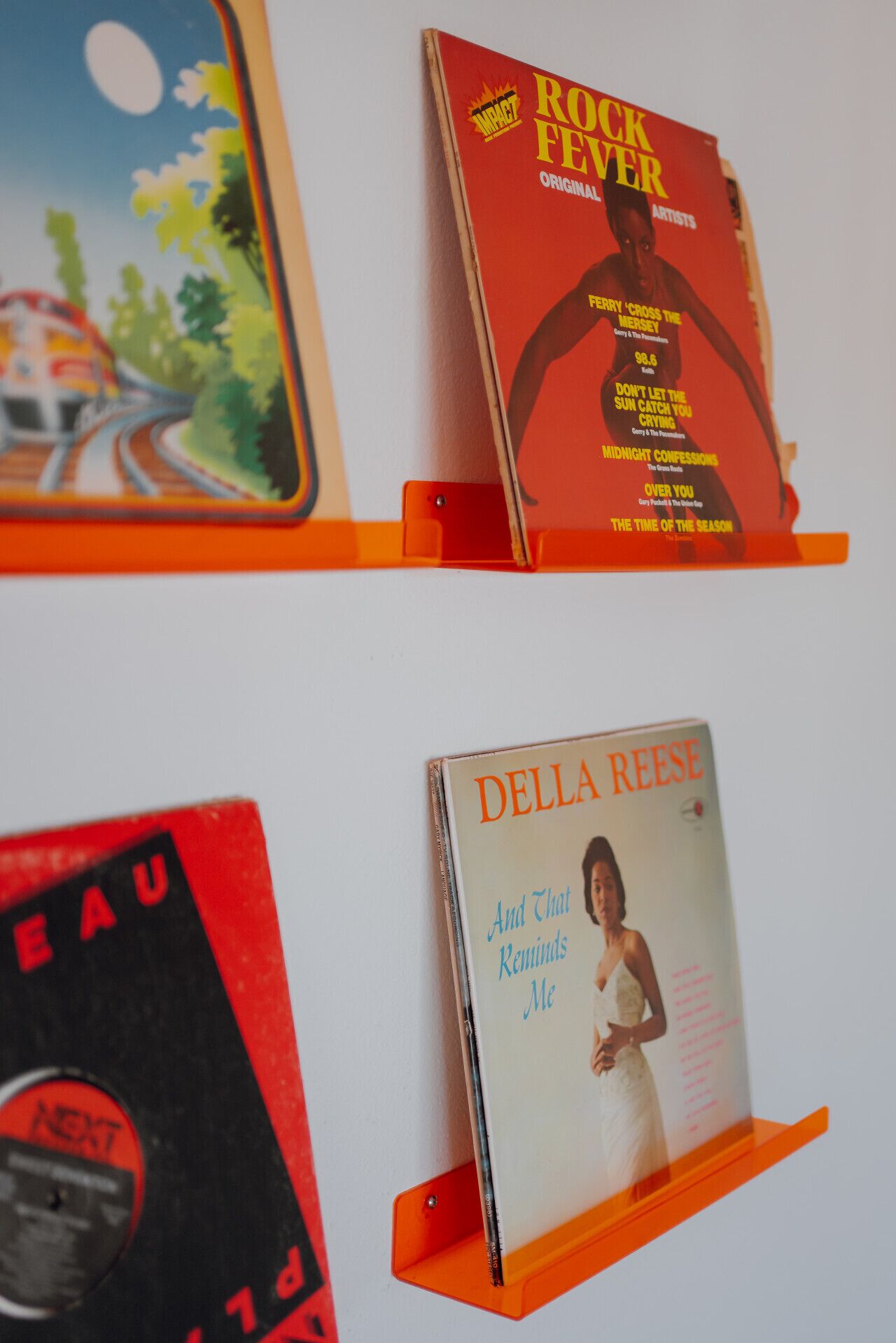 Een muur met drie vinylplaten op oranje standaardhouders.