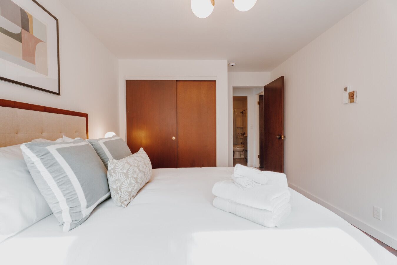 Camera d'albergo con un letto, cuscini, un armadio in legno e un bagno visibile attraverso una porta aperta.