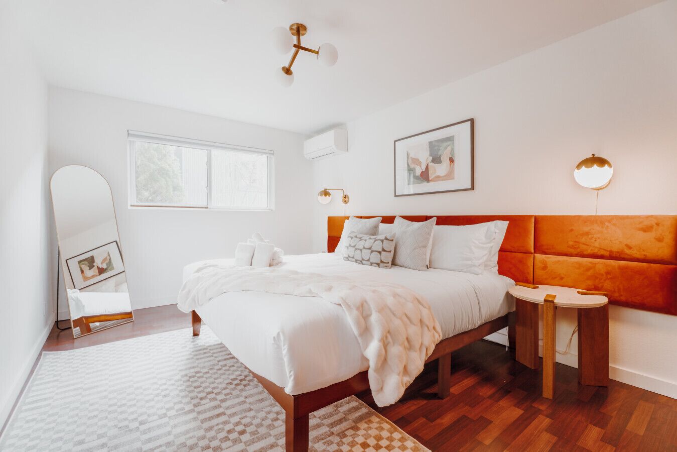Un dormitorio moderno con una cama grande, cabecera de madera, mesita de noche y una lámpara de pared.