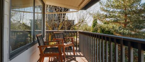 A wooden deck with two chairs and a table, a railing, and a view of trees and a building.