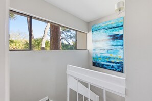 A room with a window overlooking trees, a white crib, and a large abstract painting on the wall.