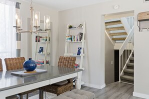 A dining area with a table, chairs, a vase, and a bookshelf.