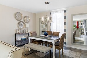 Uma sala de jantar com uma mesa branca, cadeiras de vime, um vaso azul e um candelabro.