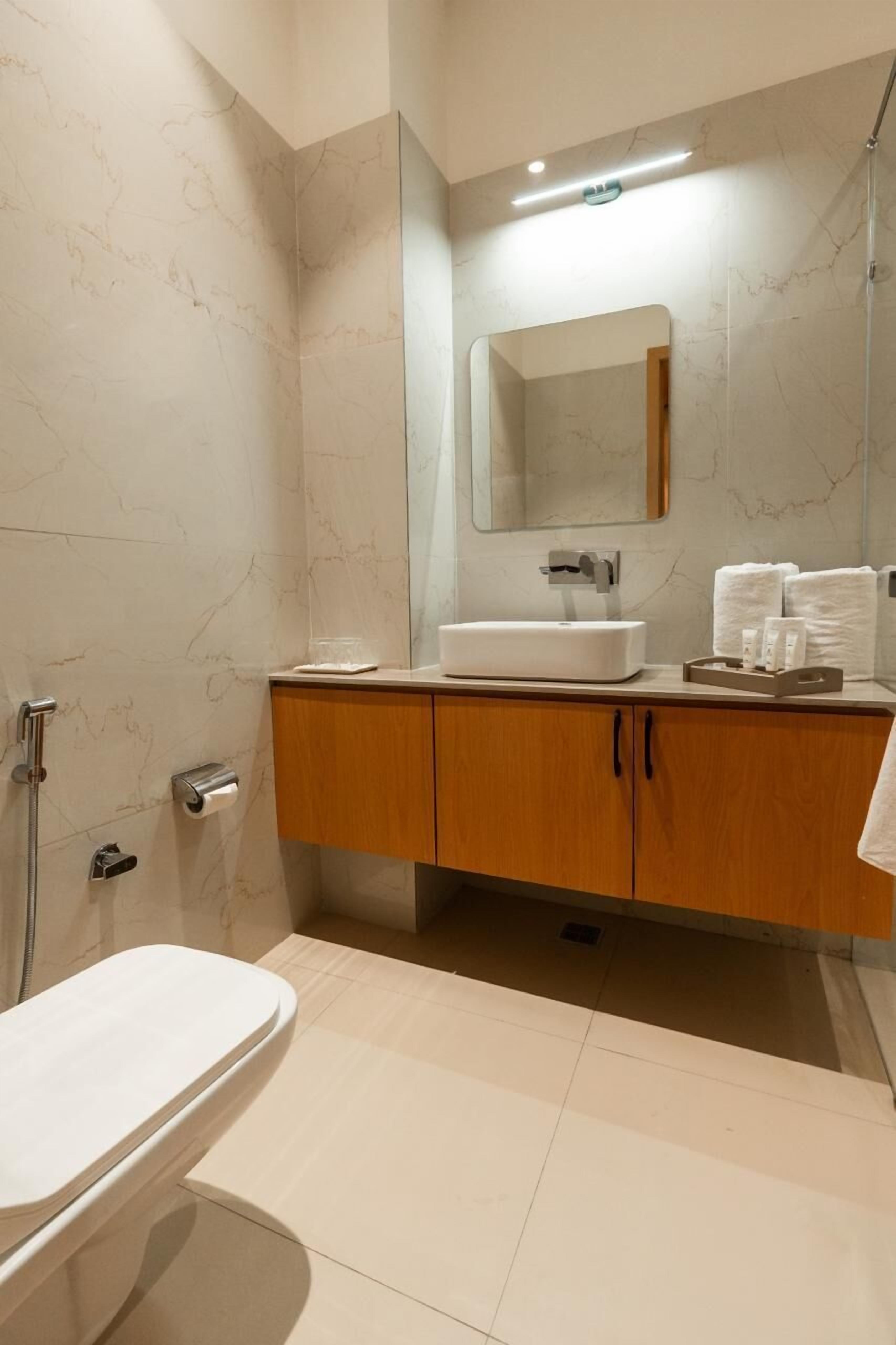 A modern bathroom with a marble wall, a wooden vanity, a white sink, and a shower area.