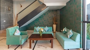 A modern living room with teal sofas, a wooden coffee table, and a staircase. - Xenious Micro (Amritsar)