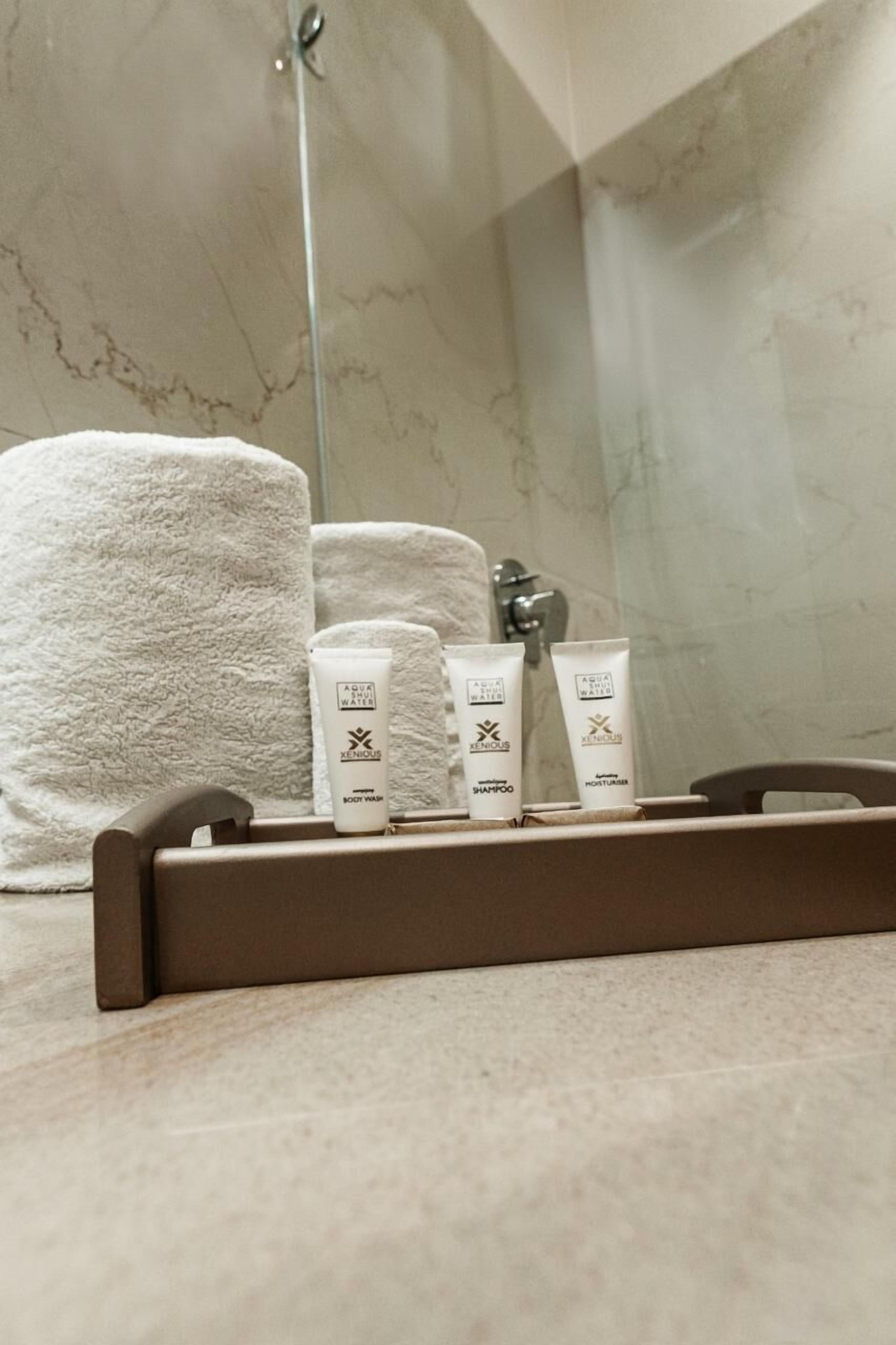 Un baño con pared de mármol, una toalla blanca y tres artículos de tocador sobre una bandeja.