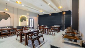 A modern dining area with wooden tables and chairs, pendant lighting, and a buffet line with metal serving dishes. - Xenious Micro (Amritsar)