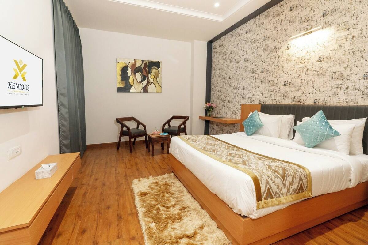 A hotel room with a large bed, a small desk, two chairs, a painting on the wall, and a textured wallpaper.