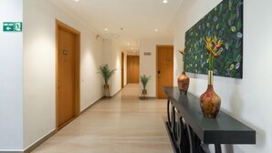 A hotel hallway with wooden doors, potted plants, a black console table with vases, and a painting on the wall. - Xenious Micro (Amritsar)