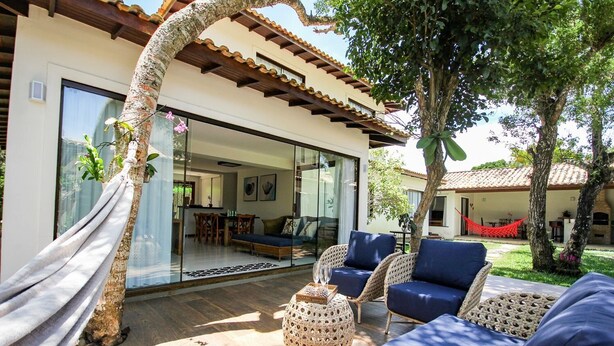 A modern outdoor living area with wicker furniture, a hammock, and a glass door leading to an interior space. - Bz44 200 metros da praia Área Gourmet (Buzios)