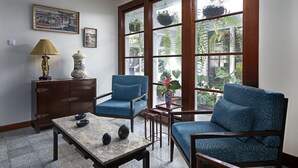 A room with a large window, two blue armchairs, a wooden cabinet, a table, and decorative items.