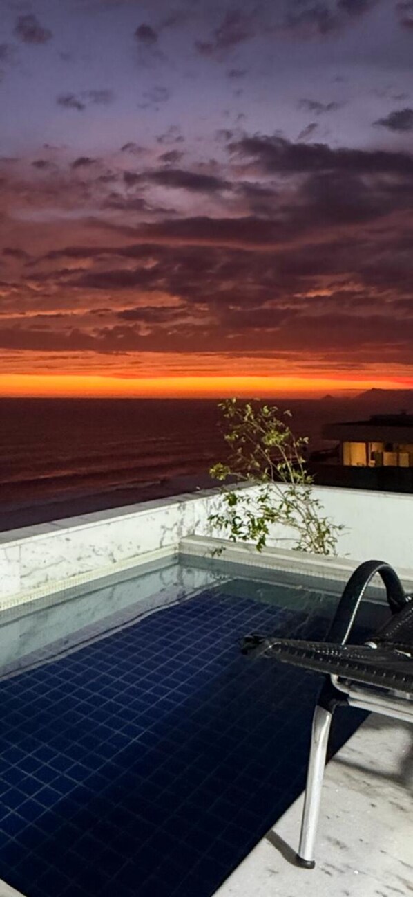 A rooftop pool with a view of the ocean at sunset.