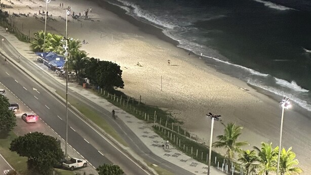 Una playa con una carretera que bordea la orilla, palmeras y una vista despejada del océano.