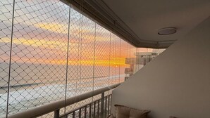 Un balcón con vistas a la puesta de sol sobre el agua, una zona de estar con cojines y una barandilla.