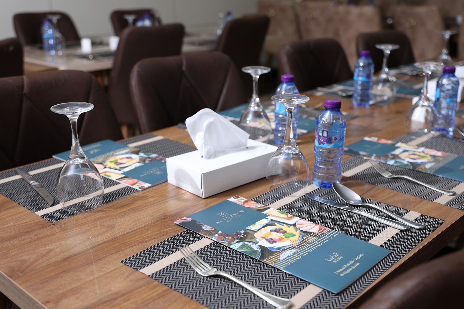 Une salle de conférence avec une longue table préparée pour une réunion, équipée de bouteilles d’eau, de verres et d’une boîte de mouchoirs.