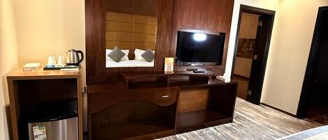 Habitación de hotel con cama, escritorio con televisor de pantalla plana, minibar y espejo grande.
