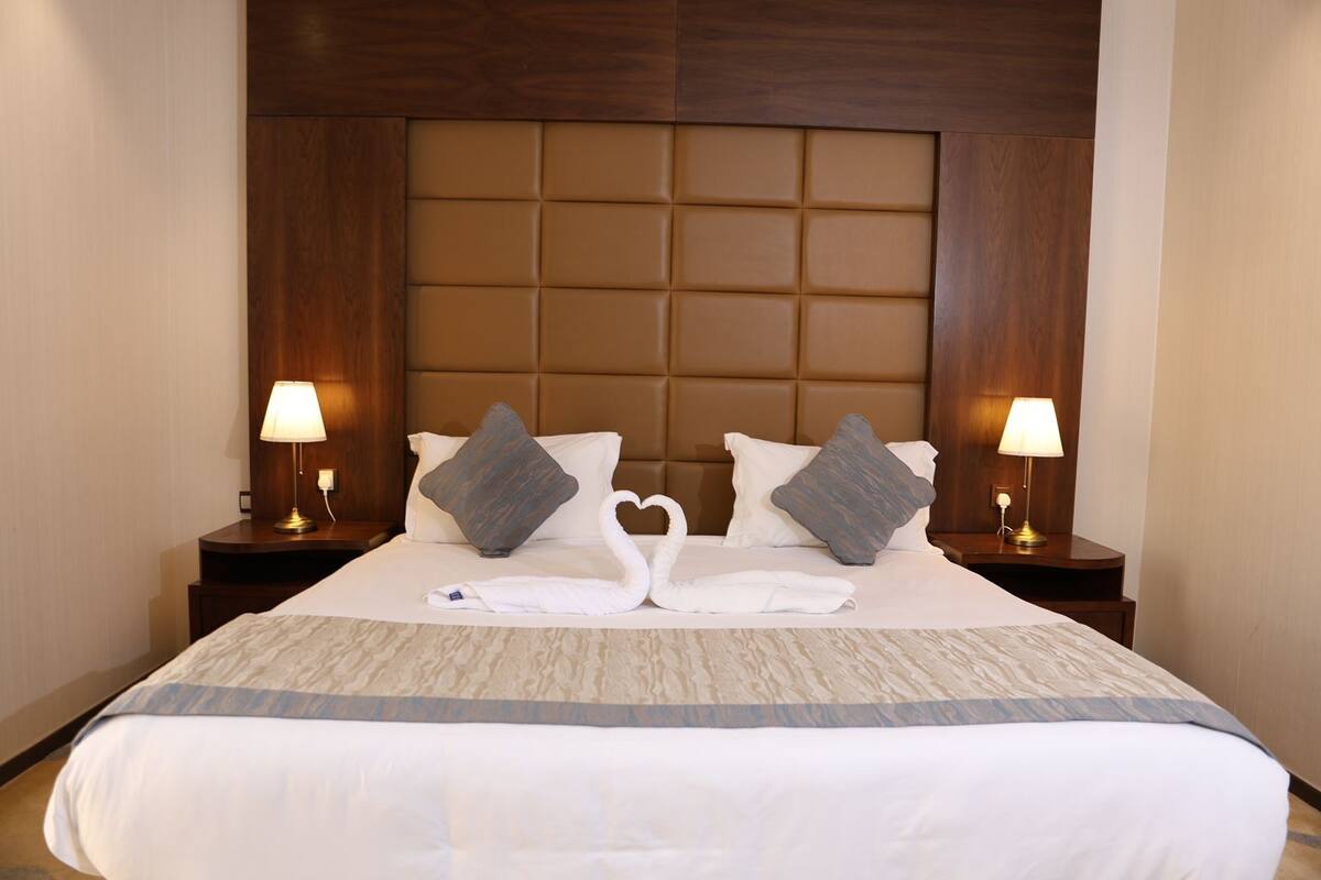 A hotel room with a large bed, two nightstands, two lamps, and a headboard with a padded panel.