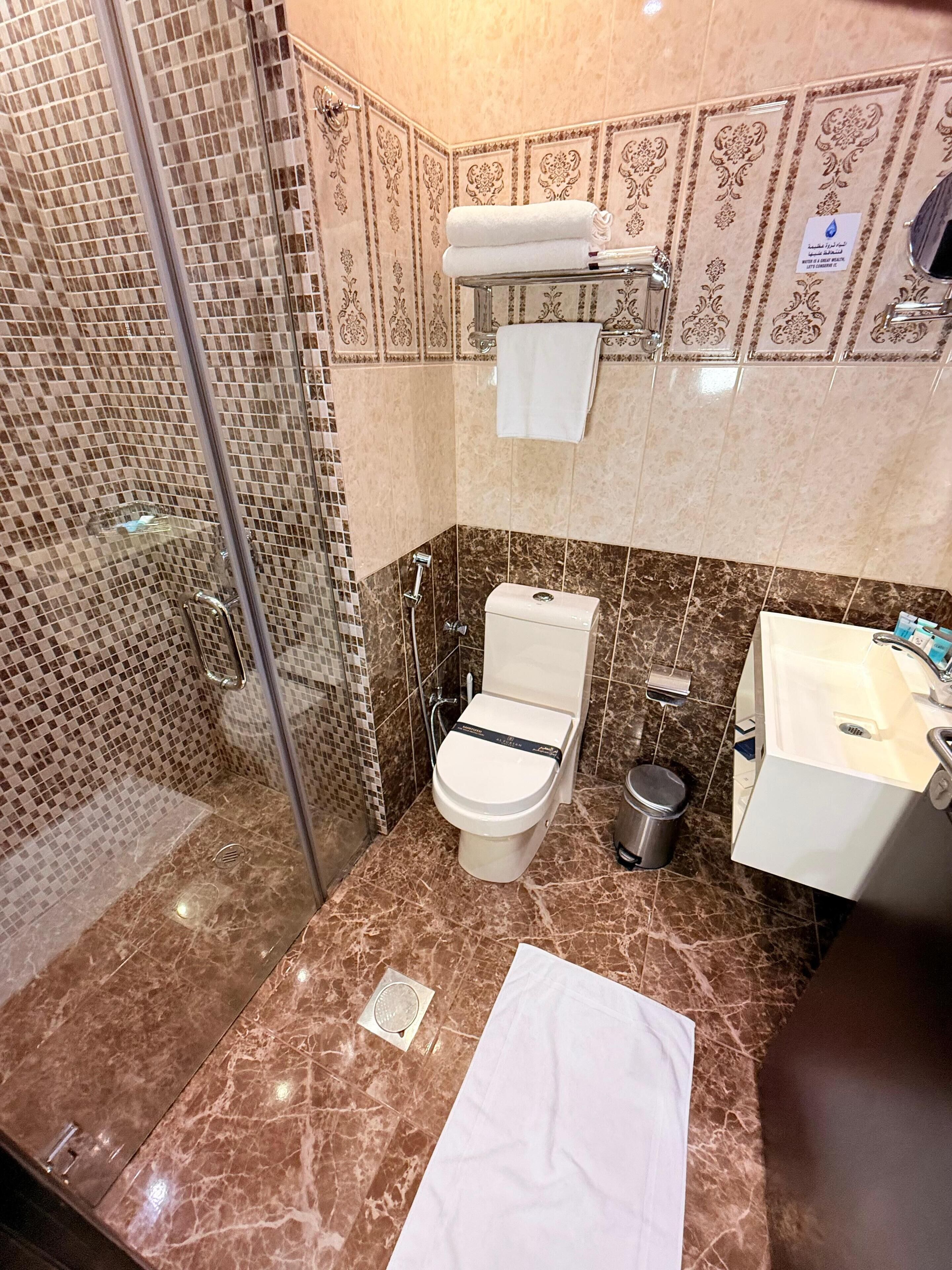 A bathroom with a glass shower enclosure, a toilet, a sink, and a trash can.
