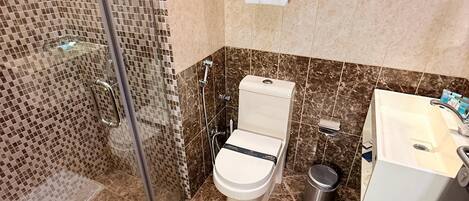 A bathroom with a glass shower enclosure, a toilet, a sink, and a trash can.