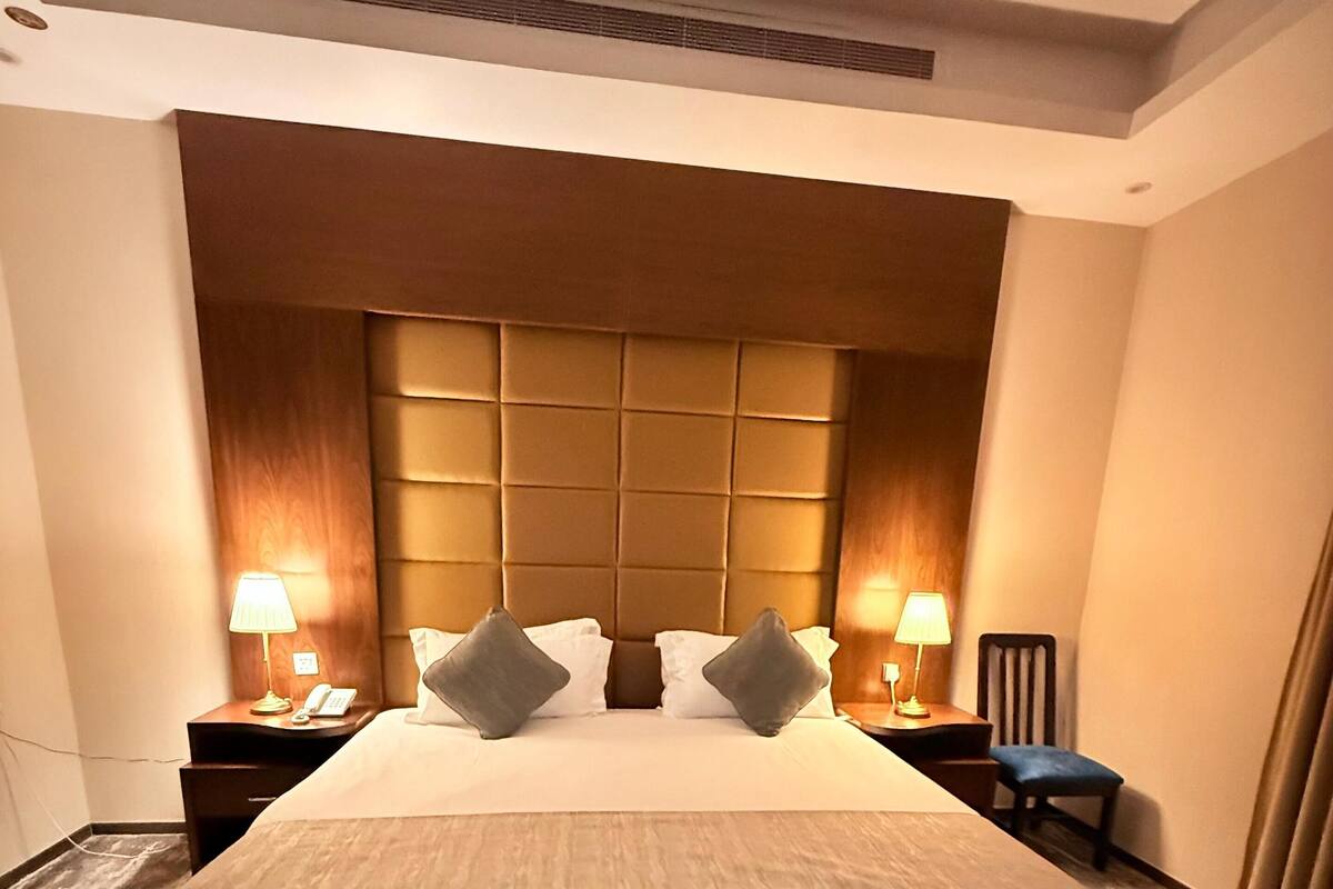 A hotel room with a large bed, two bedside tables with lamps, a wooden headboard, and a wooden floor.