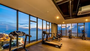 Un gimnasio con cintas de correr y bicicletas estáticas, amplias ventanas con vistas a la ciudad y montañas.