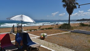 A beachside area with a white umbrella, lounge chairs, and a palm tree. - Cielo Chania II (Chania)