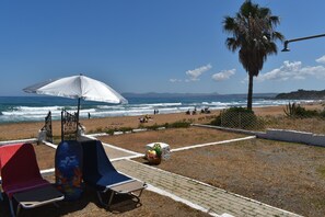 A beachside area with a white umbrella, lounge chairs, and a palm tree.