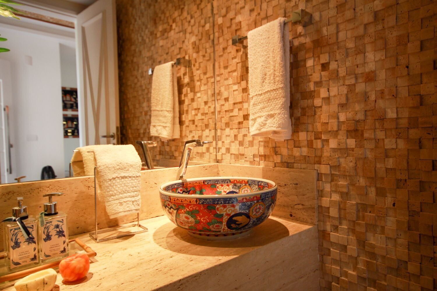 Un baño con pared de mosaico, un lavamanos con un cuenco decorativo y dos toallas colgadas en la pared.
