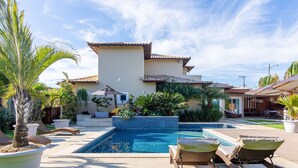 Un área de piscina con sillones reclinables y plantas en macetas.
