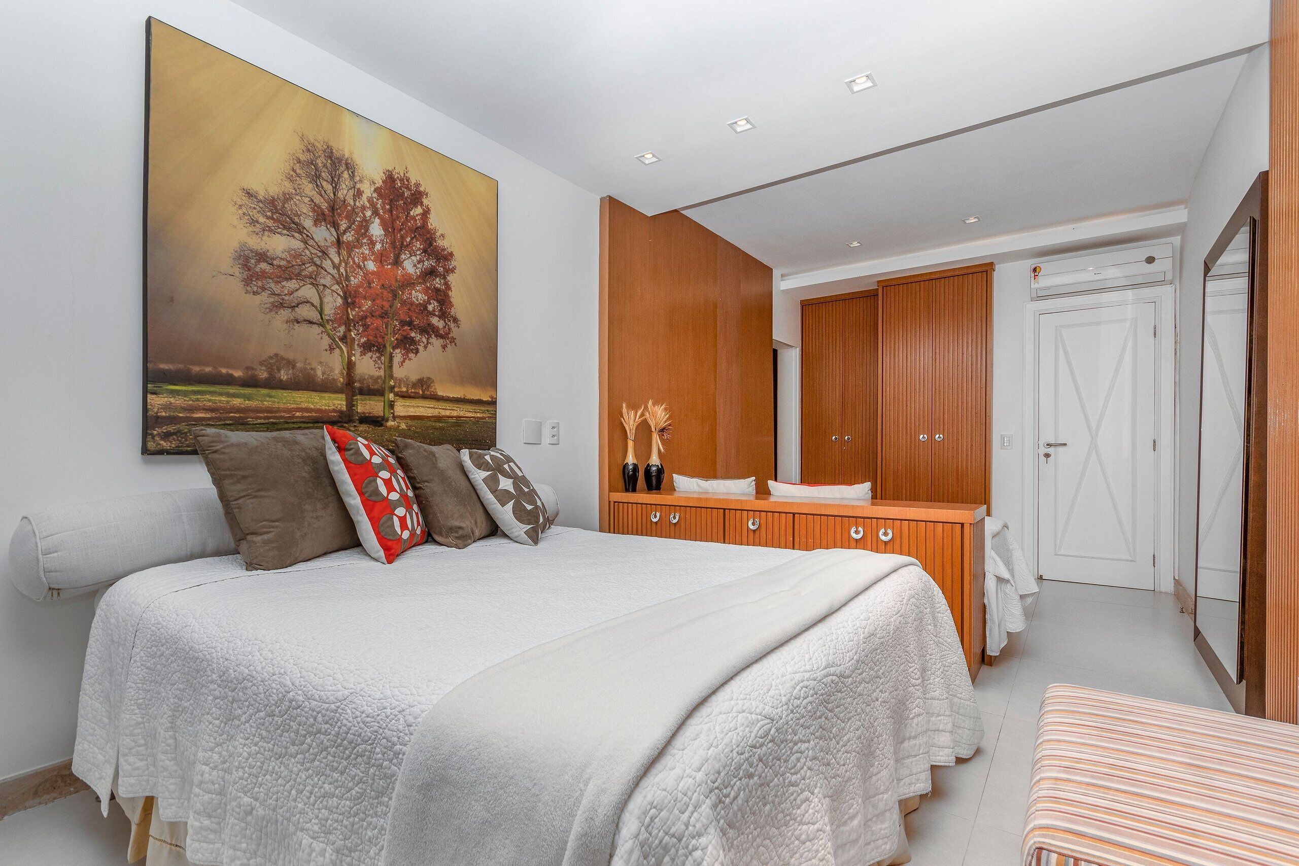 A bedroom with a large bed, a wooden dresser, a mirror, and a door.