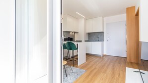 A modern kitchen with white cabinets, a granite countertop, and a bar area with a green chair. - Infante Studio w/ Parking by LovelyStay (Vila Nova de Gaia)