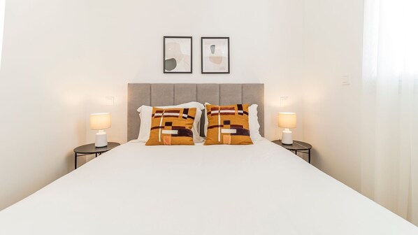Una camera d'albergo con un letto grande, due comodini con lampade e due dipinti astratti alle pareti.