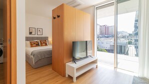 A modern bedroom with a bed, a TV on a stand, a wardrobe, and a balcony with a city view. - Infante Studio w/ Parking by LovelyStay (Vila Nova de Gaia)