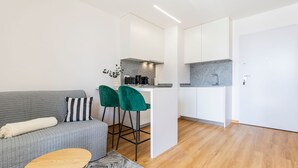 A modern apartment with a grey sofa, two green bar stools, a kitchen area with a granite countertop, and a white door. - Infante Studio w/ Parking by LovelyStay (Vila Nova de Gaia)