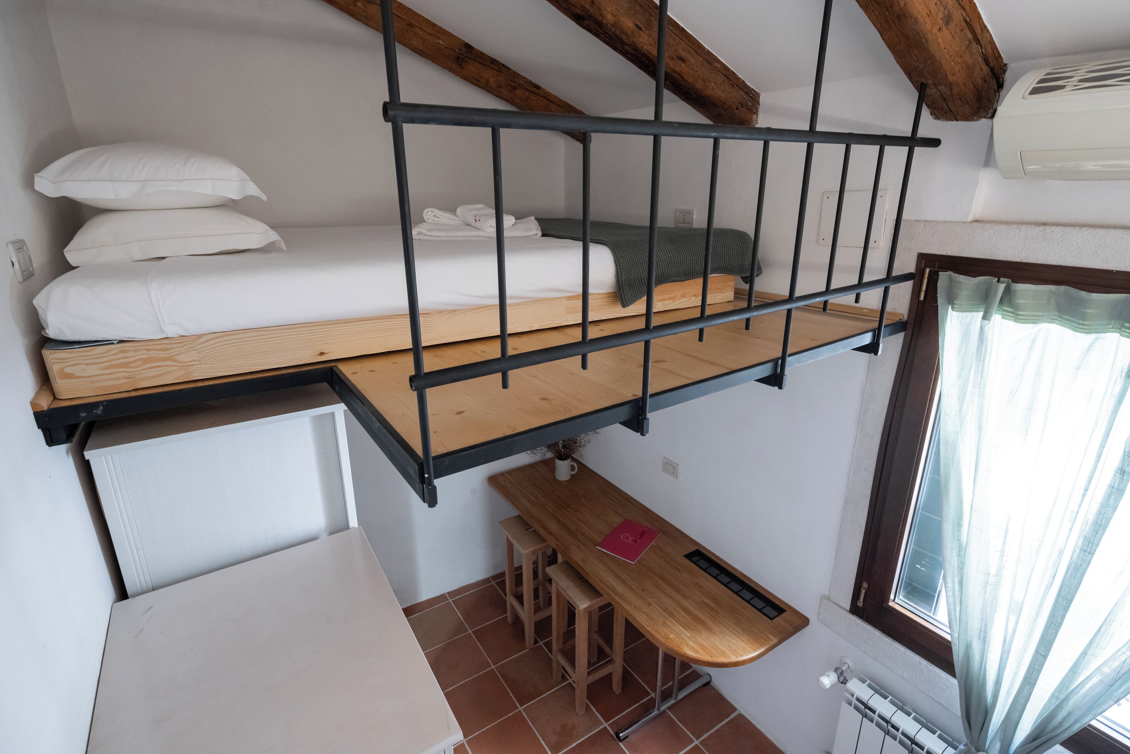 Habitación compacta con cama en literas, una pequeña mesa de madera y ventana con cortinas.