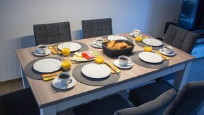 Una mesa de desayuno dispuesta con platos, tazas y una cesta de cruasanes, junto con zumo de naranja y café.