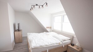 Un dormitorio con techo inclinado, una cama de madera, una mesita de noche con lámpara y un armario pequeño.