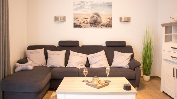 Una sala de estar moderna con un sofá modular, una mesa de centro con bebidas, un cuadro enmarcado en la pared y una planta en maceta.