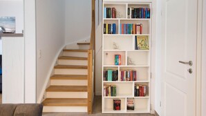 Una escalera que conduce a una habitación con una puerta blanca, una estantería blanca llena de libros y un sofá marrón en primer plano.