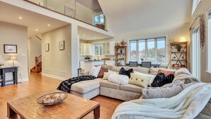 A spacious living area with a high ceiling, a large window offering a view, a kitchen with white cabinets, and a staircase leading to an upper level. - EXECUTIVE WATERFRONT LIVING AT ITS FINEST!!! WELCOME to this immaculate home! (Wasaga Beach)