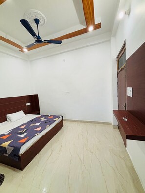 A bedroom with a bed, a ceiling fan, a wooden headboard, a wardrobe, and a marble floor. - Ahem Palace Home Stay (Faizabad)
