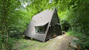 A small, dark-colored cabin with a sloped roof, surrounded by dense green foliage. - Chalet Séquoia 138, Chalet Durbuy Family, nature, swimming pool dogs welcome (Durbuy)