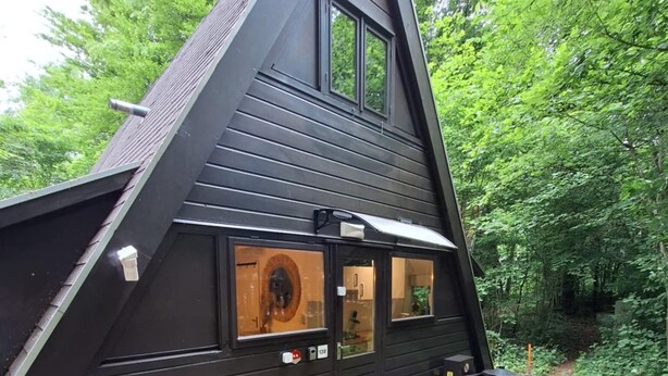 A black wooden cabin with a triangular roof, large windows, and a small patio area with potted plants. - Chalet Séquoia 138, Chalet Durbuy Family, nature, swimming pool dogs welcome (Durbuy)
