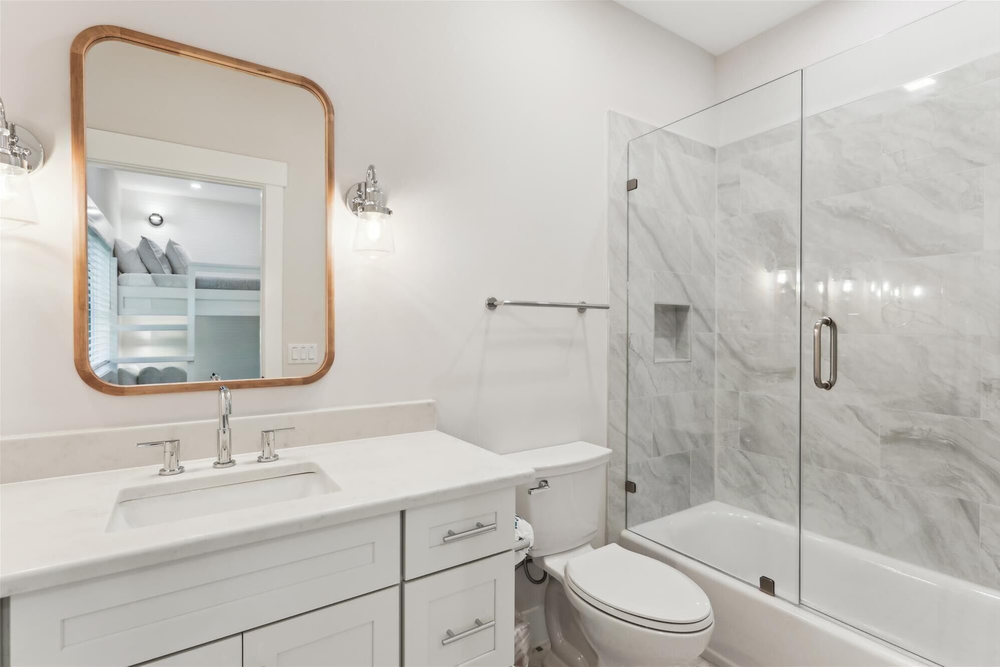 A modern bathroom with a white vanity, a large mirror with a wooden frame, a glass shower enclosure, and a white toilet.