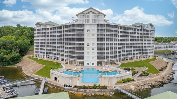 A large, multi-story hotel with a central courtyard featuring a swimming pool, surrounded by water and greenery. -  2110 Towers Beautiful Condo! Quiet! Elevators, indoor/outdoor pools. Free Wifi (Osage Beach)