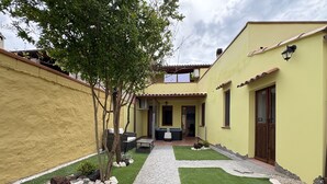 A courtyard with a paved walkway, a seating area, and a small garden with rocks and a tree.