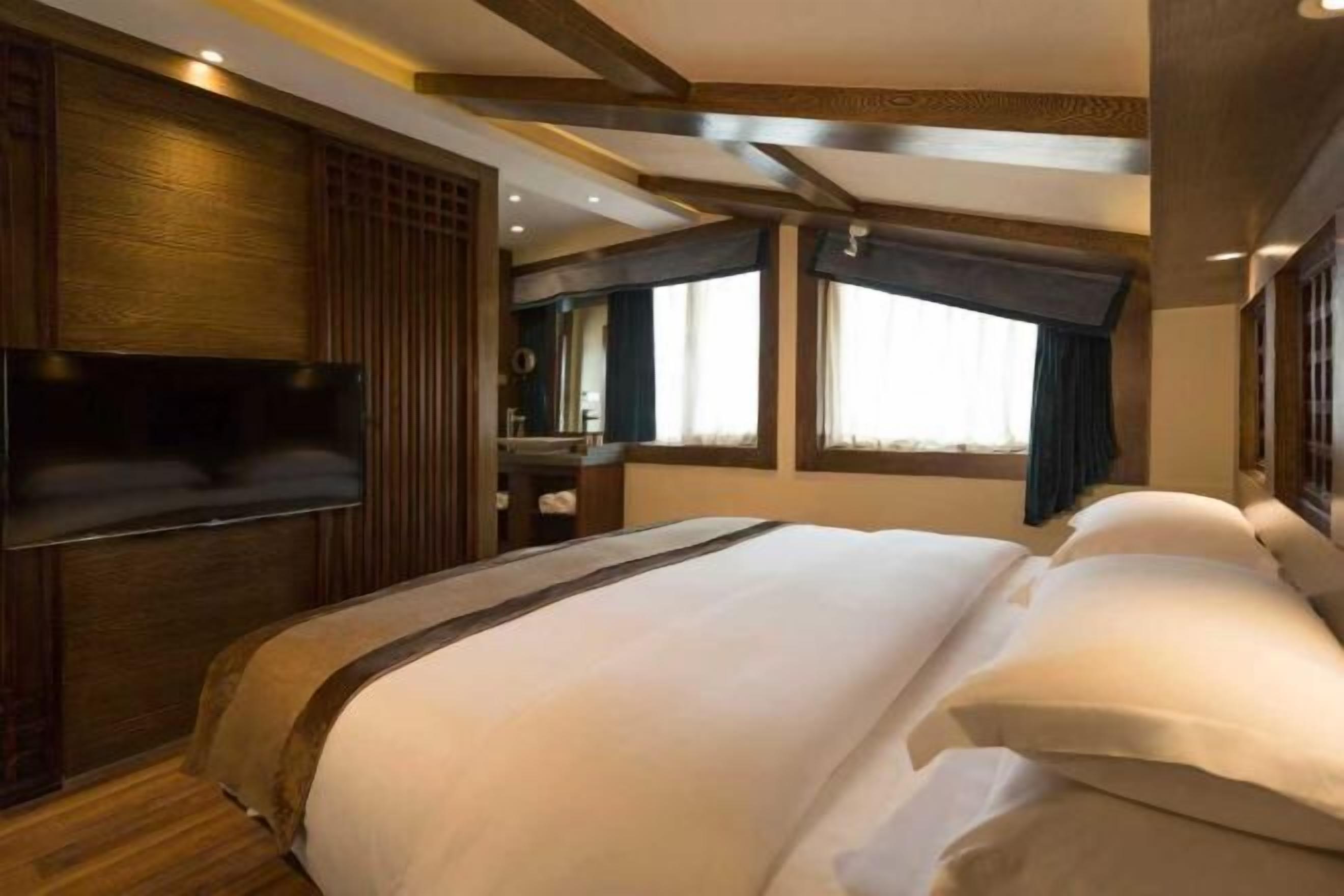 Habitación de hotel con una cama grande, paneles de madera, un televisor de pantalla plana y una ventana con cortinas.
