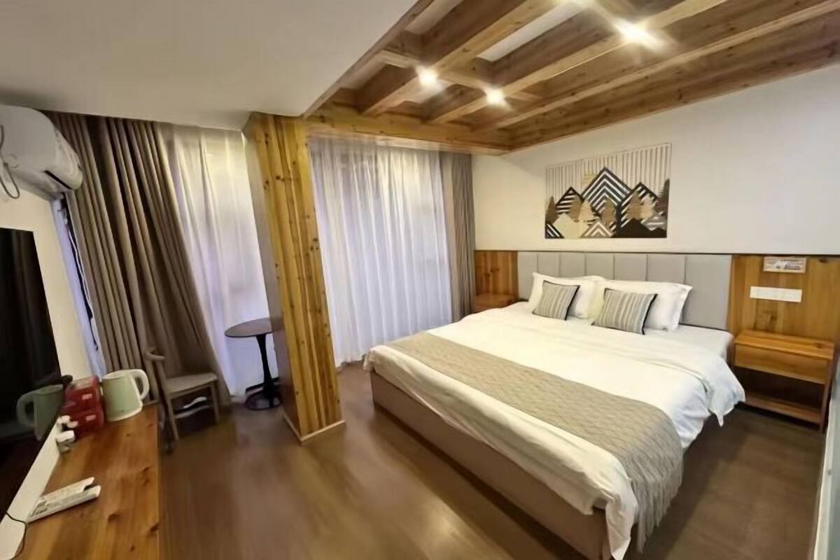 Ein Schlafzimmer mit Holzbalkendecke, einem Bett mit weißer Bettwäsche, einem Schreibtisch mit Stuhl und einem Fenster mit Vorhängen.