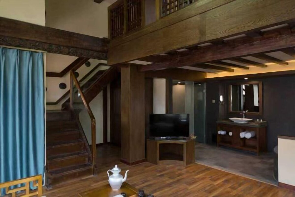 A spacious living area with a wooden staircase, a flat-screen TV, and a bathroom with a sink and mirror.