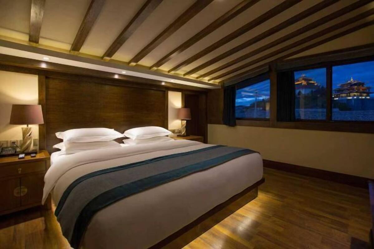 Ein Hotelzimmer mit einem großen Bett, Holzbalkendecke, Nachtblick auf ein Gebäude und einem Nachttisch mit Lampe.